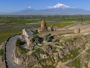 Historic church in a wide landscape in front of impressive mountain peaks under a clear sky, aerial