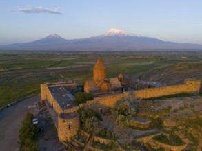 Historic monastery with surrounding wall and view of Mount Ararat at sunrise, aerial view, Chor