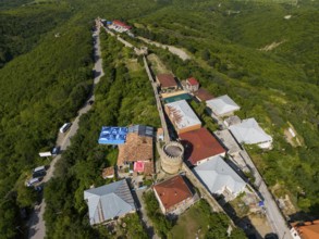 View of a village along a stone wall with towers, embedded in green hills and forests, aerial view,
