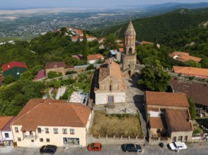 Village view with church tower and brick buildings, surrounded by green hills and wide landscape,