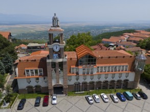 Large building with clock tower and surrounding traditional roofs on a slope, aerial view, town