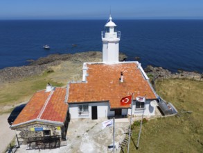 A lighthouse with terracotta roof on a rocky coast with flags and a wide ocean in the background,
