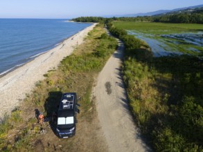 A van parked on a beach along a coastal road with lush vegetation and sea view, aerial view,