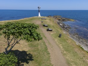 Path leading to a lighthouse on the coast, surrounded by trees and benches in a summer landscape,