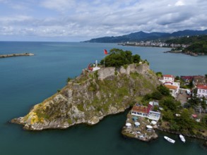 Castle on a rock formation near coastal houses and mountains with clouds, aerial view, fortress,