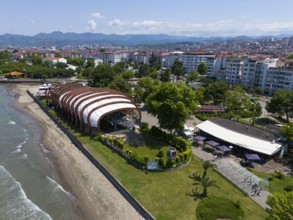 Coastal view with event hall next to beach and modern buildings in an urban environment, aerial