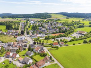 Aerial view of a village in the middle of a green landscape with numerous houses and fields under a