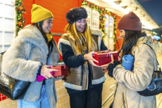 Three joyful women exchanging christmas gifts while enjoying the festive atmosphere of a