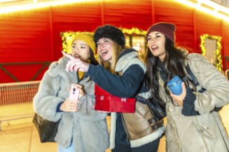 Three young women holding christmas gifts and a smartphone are enjoying the christmas spirit,