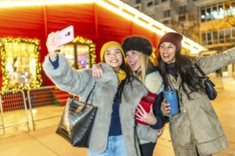 Three happy female friends taking a selfie at a christmas market, enjoying the festive atmosphere