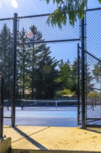 Open black metal gate of a blue pickleball court illuminated by the summer sun, inviting players to