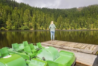 Pedal boats and a person on a jetty on the lakeshore, surrounded by forest, Mummelsee, Seebach,