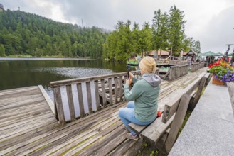 Woman at the lake photographed with her smartphone from a wooden jetty, Mummelsee, Seebach, Ortenau
