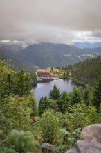 View over a lake with mountains and houses under a cloudy sky, Mummelsee, Seebach, Ortenau