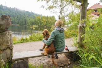 Woman with dog on a bench by the lake in the countryside, relaxed atmosphere in nature, Mummelsee,