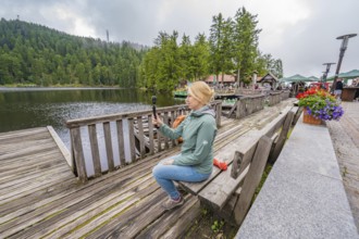 Woman on a wooden footbridge next to a lake with a camera in her hand, Mummelsee, Seebach, Ortenau
