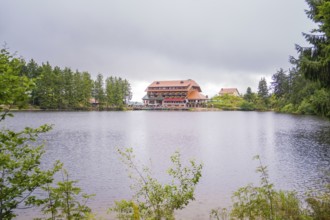 A hotel on the shore of a lake, surrounded by forest and overcast skies, Mummelsee, Seebach,