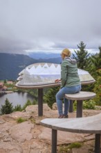 Woman sitting at a viewpoint and looking at the lake and forest landscape in the mountains,