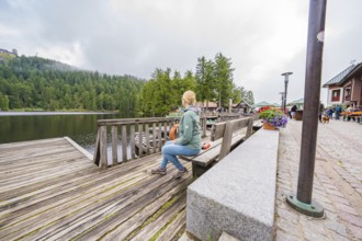Woman on a bench next to a lake and flowers on a wooden footbridge, Mummelsee, Seebach, Ortenau