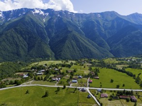 A small village in the middle of a vast green landscape with high mountains in the background,