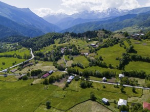 Hilly landscape with small settlements and green fields surrounded by mountains, aerial view,