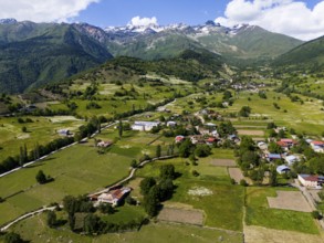 Mountain landscape with scattered villages and green meadows under a blue sky with clouds, aerial