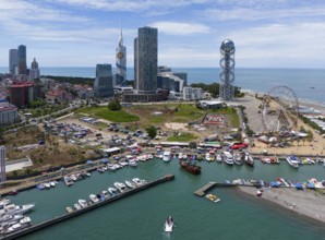 Harbour city with yachts, skyscrapers and a Ferris wheel on the coast in sunny weather, aerial