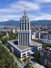 A tall modern building in an urban environment with mountains, aerial view, Sheraton Hotel, Batumi,