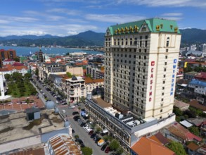 Large hotel building in a coastal town with mountains in the background and lively street scene,