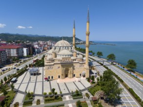 Panoramic view of a large mosque with minarets on a coastline flanked by streets and buildings,