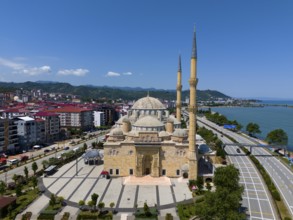 Large mosque with several minarets on the coast, surrounded by modern buildings and mountains in
