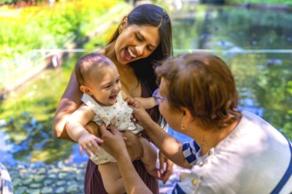 Happy latin family enjoying a sunny day in a park, mother holding her baby while grandmother is