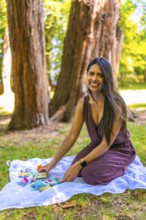 Latin mother arranging colorful baby toys on a blanket in a park, enjoying a sunny day outdoors