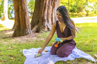Latin mom arranging colorful baby toys on blanket in park, enjoying quality time with her child in