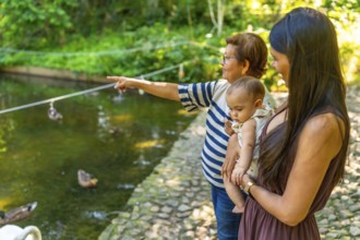 Grandmother joyfully pointing at ducks while enjoying a sunny day at the park with her daughter and