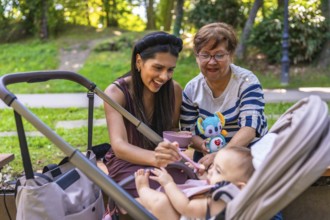 Grandmother, mother and baby girl enjoying time together at the park, feeding the baby girl and