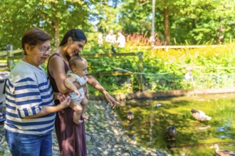 Grandmother, mother, and granddaughter enjoying a sunny day at the park, observing ducks swimming