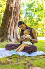 Latin mother and daughter spending time together in a park, playing with toys on a blanket under a