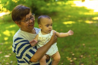 Smiling grandmother cradling her adorable granddaughter in a vibrant green park, enjoying a sunny