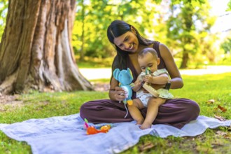 Latin mother and her baby daughter enjoying playtime with colorful toys while sitting on a blanket