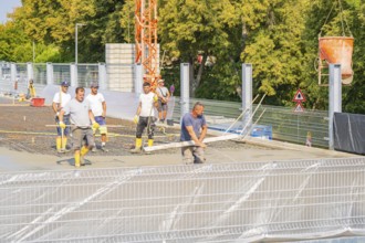 Group of construction workers on a building site with warning signs and a crane nearby, car park
