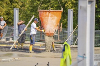Two workers pouring concrete from large mixer tubs, surrounded by safety measures and mesh fencing,