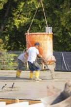 Two construction workers pouring concrete from a concrete mixer on a building site, surrounded by