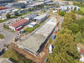 Large-scale construction site with crane and buildings in green, urban surroundings, car park