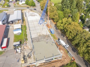 Aerial view of a construction site with crane and concrete foundation, surrounded by trees in