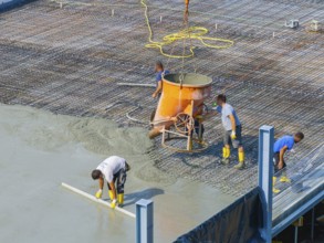 Workers pouring concrete on a construction site with concrete mixer and steel frame structure in