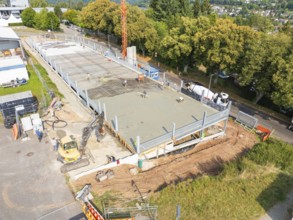 Construction site with concreted area, machines and construction workers, surrounded by green