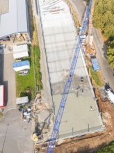 Aerial view of a construction site with blue crane and concrete surface next to a road, car park