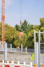 Crane lifts a concrete bucket over an almost finished building site. Two construction workers,
