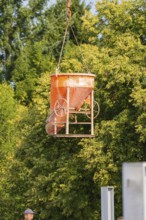 Concrete mixer being lifted with a crane on a construction site near trees, car park construction,